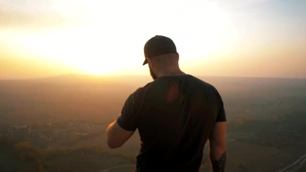 穿着黑色T恤的游客站在悬崖顶上欣赏金色的落日 — 图库视频影像
