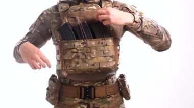 Multicam kamuflajlı özel harekat subayı dolu tüfek şarjörlerini, beyaz arka planlı plaka taşıyıcısının çantalarına yerleştirir.