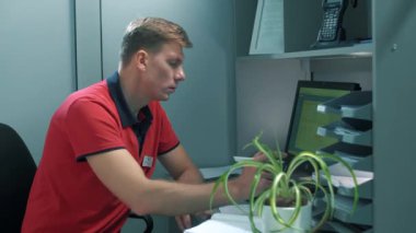 Müdür bir ofis kabininde çalışır, satış verilerini bilgisayar veritabanıyla bağdaştırır ve bunları özel bir deftere yazar.