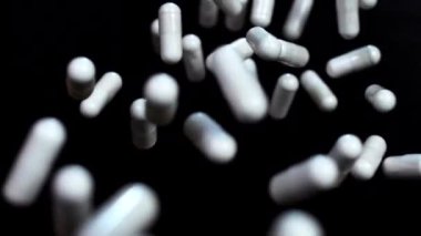 Vitaminlerin beyaz kapsülleri yukarı uçar ve siyah arka plana karşı ağır çekimde havada süzülür. Makro