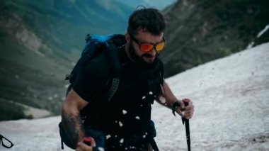 Şık gözlüklü, tırmanış ekipmanlarıyla sakallı bir dağcı dağlarda bir buzulun üstünde yükseliyor. Yavaş çekim