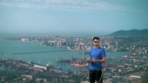一个体格健壮的年轻人站在山顶上 有一个四合院的控制板 俯瞰着整个城市 — 图库视频影像