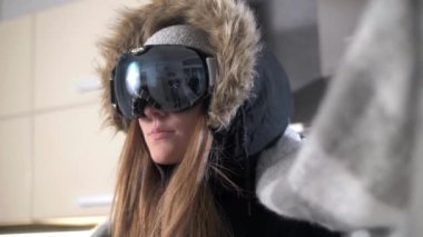 Snowboard yapmak için gözlüklü genç bir kız kafasına sıcak bir eşarp örüyor.