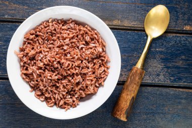 Kasedeki kırmızı pirinç mavi ahşap arka planda izole edilmiş kaşık yakın, üst manzara, Asya yemekleri ve içecek konsepti var..