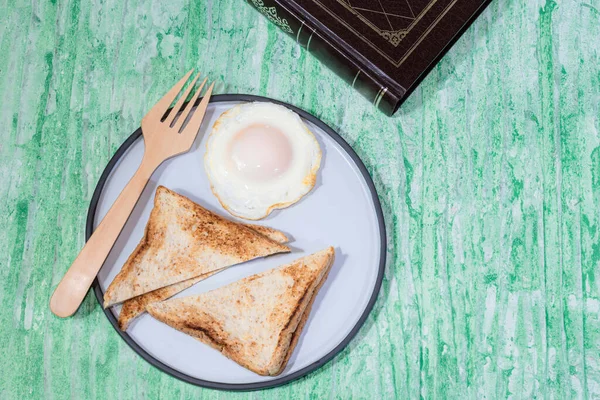 プレートの目玉焼きパンは緑の背景に閉じ込められた本を持っています トップビュー 朝食の食べ物や飲み物の概念 — ストック写真