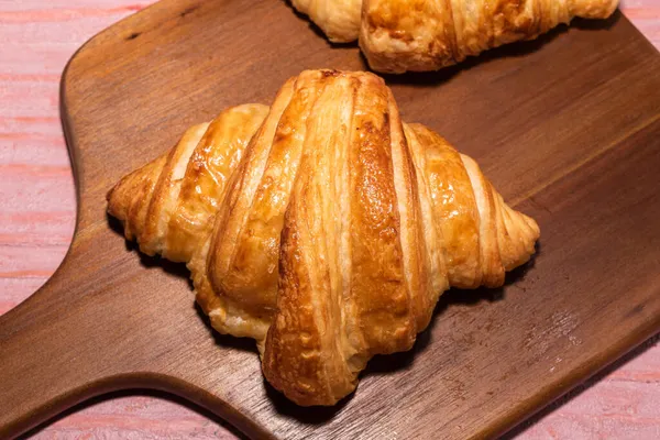 Twee Croissant Snijplank Geïsoleerd Roze Houten Achtergrond Close Bovenaanzicht Kopieerruimte — Stockfoto