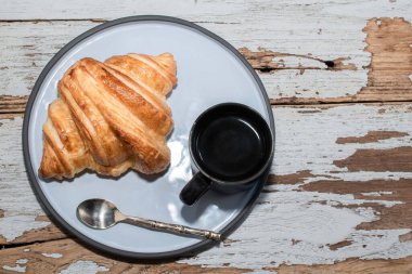 İzole edilmiş beyaz ahşap masa üzerinde espresso kahve ve kruvasan yakın plan, üst görüş, kahvaltı yemeği ve içecek konsepti.