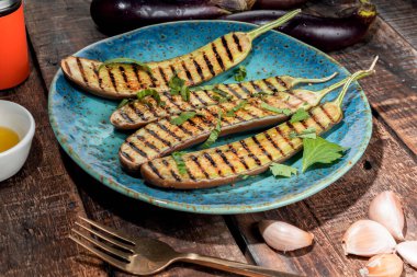 Mavi tabakta ızgara patlıcan, ahşap arka planda izole edilmiş çatal ve zeytinyağı sarımsağı var. Yakın plan, üst manzara, sağlıklı yiyecek konsepti..