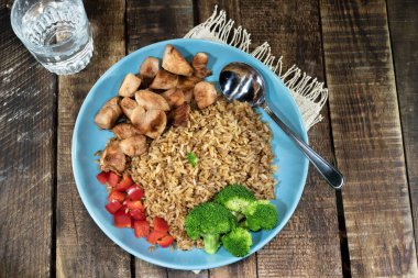 Tavuk göğsü ile kızartılmış pirinç yemeği ahşap arka planda izole edilmiş mavi tabakta sebze brokoli biberi içerir. Üst manzara, sağlıklı yiyecek ve içecek konsepti..