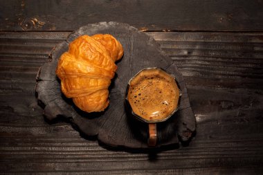 İzole edilmiş siyah ahşap masa üzerinde espresso kahve ve kruvasan yakın plan, üst görüş, kahvaltı yemeği ve içecek konsepti.