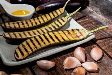 Tabakta ızgara patlıcan, ahşap arka planda izole edilmiş çatal ve zeytinyağı sarımsağı var. Yakın plan, üst görüş, sağlıklı gıda konsepti..