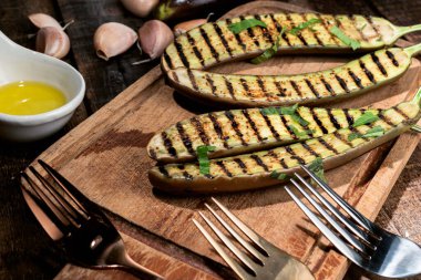 Kesme tahtasındaki ızgara patlıcanlarda çatal ve ahşap zeminde izole edilmiş zeytinyağı sarımsağı var. Yakın plan, üst görüş, sağlıklı gıda konsepti..