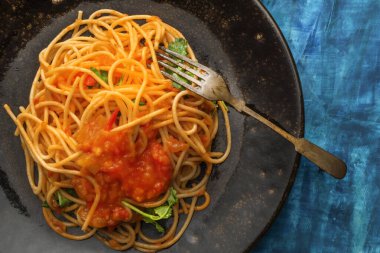 Mavi ahşap arka planda siyah tabakta domates soslu makarna, üst manzara, İtalyan yemeği konsepti..