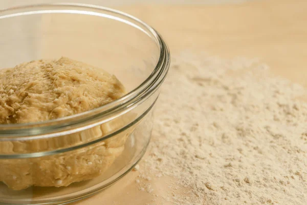 Dough in a glass dish on the table with scattered flour — Stock Photo, Image