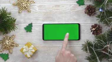 yeşil ekran teknoloji cep telefonu noel dekorasyon masasında düz görünüm, kopyalama alanı metni için makara, akıllı telefon kroma anahtarı kullanan el işi, yeni yıl online konsepti