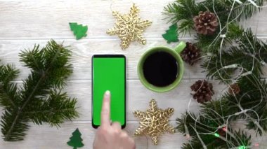 yeşil ekran teknoloji cep telefonu noel dekorasyon masasında düz görünüm, kopyalama alanı metni için makara, akıllı telefon kroma anahtarı kullanan el işi, yeni yıl online konsepti