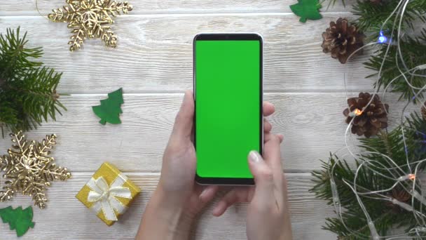緑の画面技術クリスマスの装飾テーブル上の携帯電話フラットレイアウト、コピースペーステキストのためのモックアップ、スマートフォンのクロマキーを使用して手の人、新年のオンラインコンセプト — ストック動画