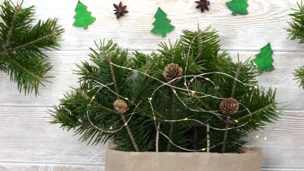 Χριστουγεννιάτικη διακόσμηση σπιτιού, κλαδιά πεύκων με γλυκάνισο και κώνους επίπεδη θέα, εορταστική σύνθεση με γιρλάντα και πράσινο φυτό σε ξύλινο τραπέζι με παιχνίδια σε σχήμα χριστουγεννιάτικου δέντρου — Αρχείο Βίντεο