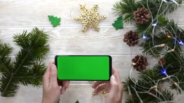 yeşil ekran teknoloji cep telefonu noel dekorasyon masasında düz görünüm, kopyalama alanı metni için makara, akıllı telefon kroma anahtarı kullanan el işi, yeni yıl online konsepti