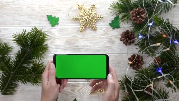 緑の画面技術クリスマスの装飾テーブル上の携帯電話フラットレイアウト、コピースペーステキストのためのモックアップ、スマートフォンのクロマキーを使用して手の人、新年のオンラインコンセプト — ストック動画