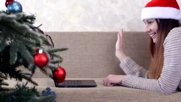 Caucásico millennial joven mujer usando santa claus sombrero celebrando vacaciones de Navidad en casa, árbol de navidad decorado rojo juguetes bolas y luces guirnalda interior — Vídeos de Stock