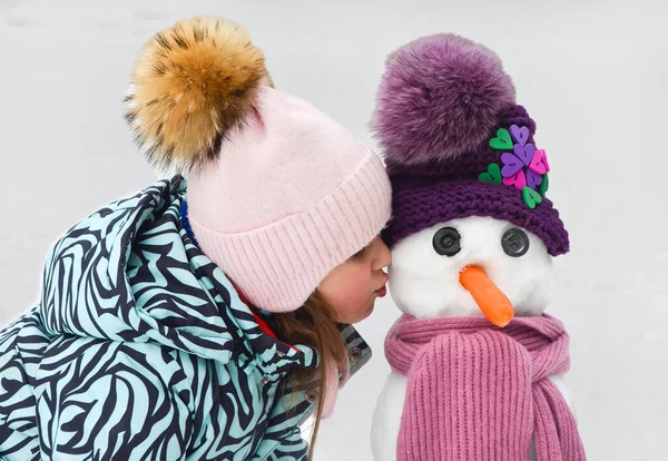 Niño caucásico en ropa de invierno jugando al aire libre con muñeco de nieve —  Fotos de Stock