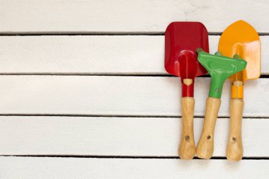 Beyaz tahtalarda ve beyaz ahşap arka planda kullanılmış renkli çocuk bahçe aletleri. Mesaj için yer. Düz yatıyordu