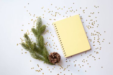 Sarı boş not defteri altın parıltılı beyaz bir Noel arkaplanındaki spirallerde. Yukarıdan bak. Mesajın için yer aç. Yeni yıl için ideal