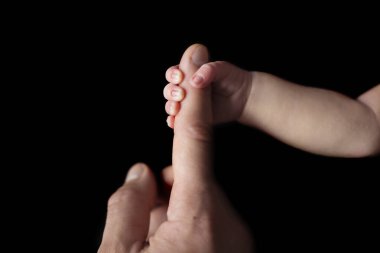 Yeni doğmuş küçük bir el, babasının parmağını siyah arka planda tutuyor. Ön Wiev