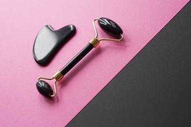 Oniks masaj guasha kazıyıcı ve pembe ve siyah arka planda yüz silindiri. Yüz bakımı için masaj aleti, SPA güzellik tedavisi konsepti. Mesaj için yer var. Düz Yatay