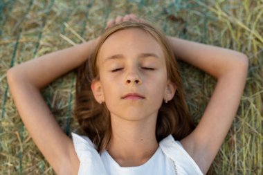A girl in a white cloth on a round haystack in the field in the wake of the sunset