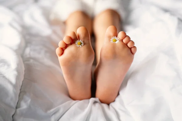 Beautiful clean feet of a little girl on a white bed with small daisies between her toes. Place for text.