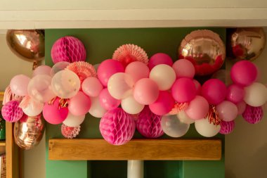 Yeşil ve bej renkli oda, bir kızın doğum günü partisi için beyaz ve şeffaf, altın renkli toplar ve kağıt dekorla süslenir..