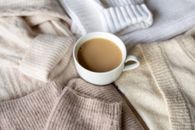 Bej örülmüş kazakların arasında beyaz bir fincan kakao. Sonbahar havası, kızlık zarı, sıcaklık ve konfor