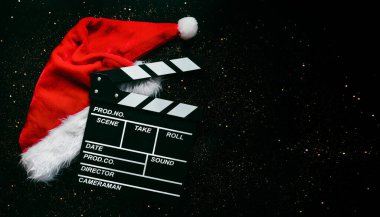 Noel Baba 'nın şapkası ve siyah arkaplandaki yazılar için parlayan parıltılarla dolu bir film tahtası. Noel filmleri konsepti