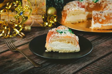 Kremalı Roscon de Reyes ve ahşap bir masada noel süsleri. Krallar Günü konsepti ispanyolca üç kralın pastası. Geleneksel İspanyol Epifani pastası. Noel için tipik İspanyol tatlısı. Seçici odak