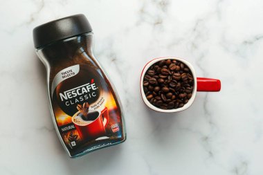 Nescafe Classic kavanozu ve mermer masada kahve çekirdekleri olan kırmızı Nescafe fincanı.