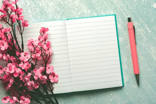 Top view of blank journal open with copy space, pink pen and almond blossoms over blue background