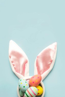 Mutlu Paskalyalar. Beyaz tavşan kulaklarına renkli paskalya yumurtası ve mavi arka planda fotokopi alanı.