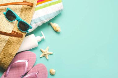 Summer holiday concept.Top view of beach bag with flip flops,beach towel,sunglasses,sea shells,sunscreen and starfish with space for text over blue background