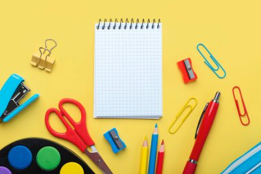Boş spiral not defteri ve sarı arkaplandaki yazı için yeri olan okul malzemelerinin üst görüntüsü. Okul konseptine dönelim.