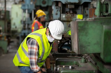 İşaretli gömlekli genç teknisyenin profil görüntüsü endüstriyel makineyi denetliyor