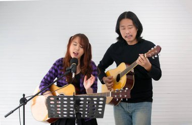 Kız mikrofonda şarkı söylüyor ve gitar çalıyor.