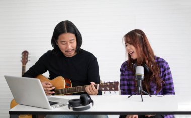 Kız mikrofonda şarkı söylüyor ve gitar çalıyor.