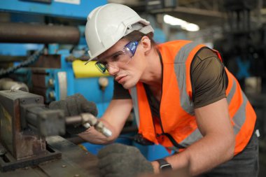 Profesyonel Ağır Sanayi Mühendisi / İşçi Güvenlik Üniforması, Gözlük ve Sert Şapka Giyen Portresi. Arka planda Odaklanmamış Büyük Endüstriyel Fabrika