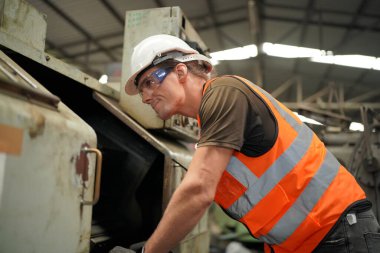 Profesyonel Ağır Sanayi Mühendisi / İşçi Güvenlik Üniforması, Gözlük ve Sert Şapka Giyen Portresi. Arka planda Odaklanmamış Büyük Endüstriyel Fabrika