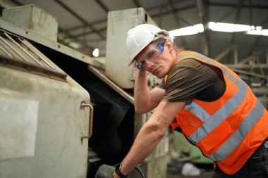 Profesyonel Ağır Sanayi Mühendisi / İşçi Güvenlik Üniforması, Gözlük ve Sert Şapka Giyen Portresi. Arka planda Odaklanmamış Büyük Endüstriyel Fabrika