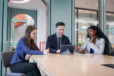Genç iş adamları ve meslektaşlarının toplantıda laptopta ve dokunmatik kağıtları tartışırken görüntüsü