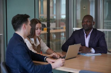 Genç iş adamları ve meslektaşlarının toplantıda laptopta ve dokunmatik kağıtları tartışırken görüntüsü