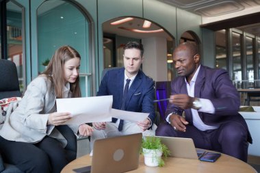 Genç iş adamları ve meslektaşlarının toplantıda laptopta ve dokunmatik kağıtları tartışırken görüntüsü
